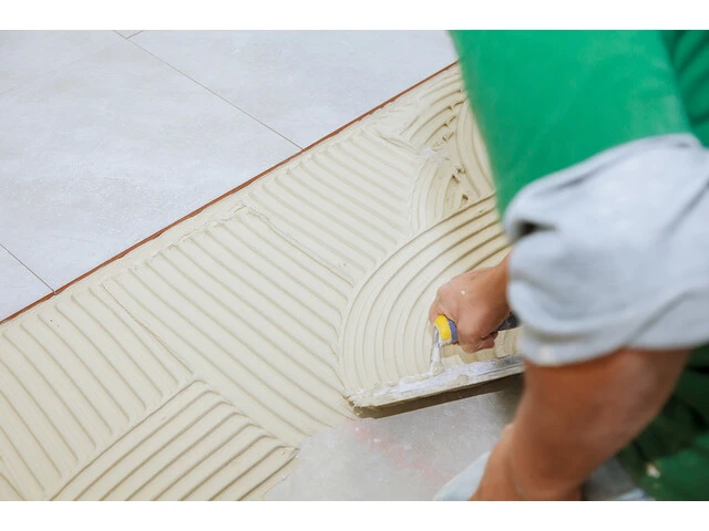 Tiling The Bathroom Floor With Tile Adhesive By Spreading The Tile Adhesive With Notch Trowel